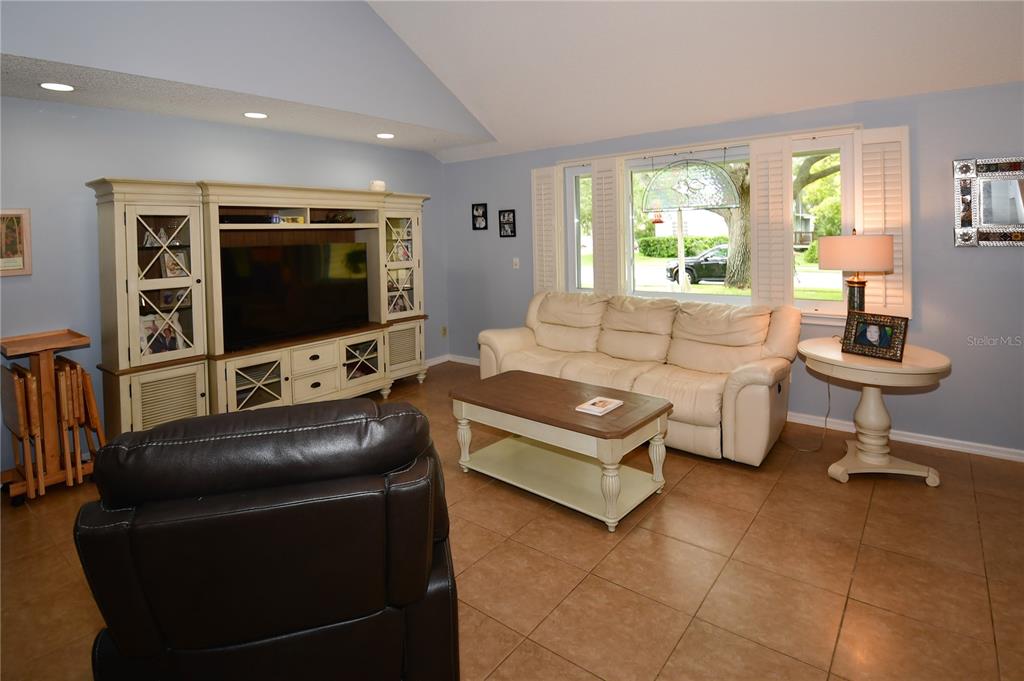A living room features a vaulted ceiling, tile flooring, a large entertainment center, and sofa — 7519 HARBOR VIEW WAY, SEMINOLE, FL