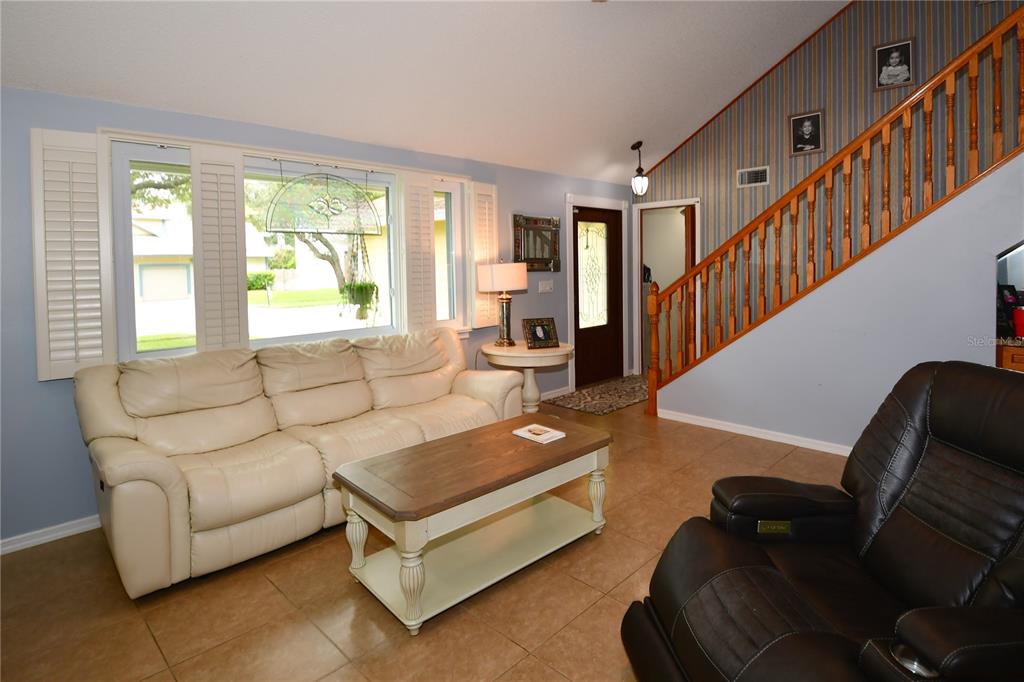 A living room features a white sofa, a dark recliner, and a staircase with wooden railings — 7519 HARBOR VIEW WAY, SEMINOLE, FL