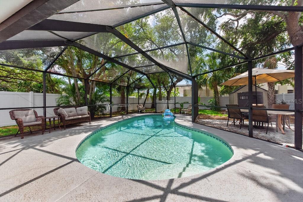 A screened-in patio features a kidney-shaped swimming pool, outdoor furniture, and surrounding trees — 1715 S HUBERT AVENUE, TAMPA, FL