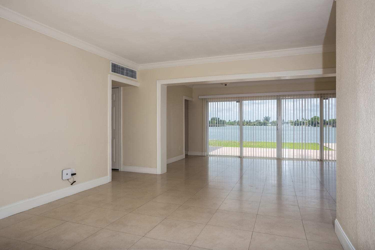 An empty room with beige tile flooring and sliding glass doors overlooking a lake — MIAMI, FL