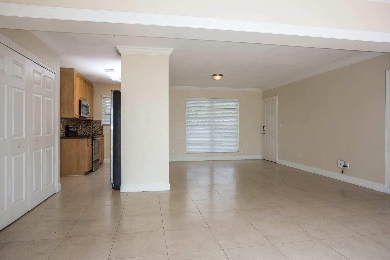 An open-concept living area features beige tile flooring, a kitchen, and a window with blinds — MIAMI, FL