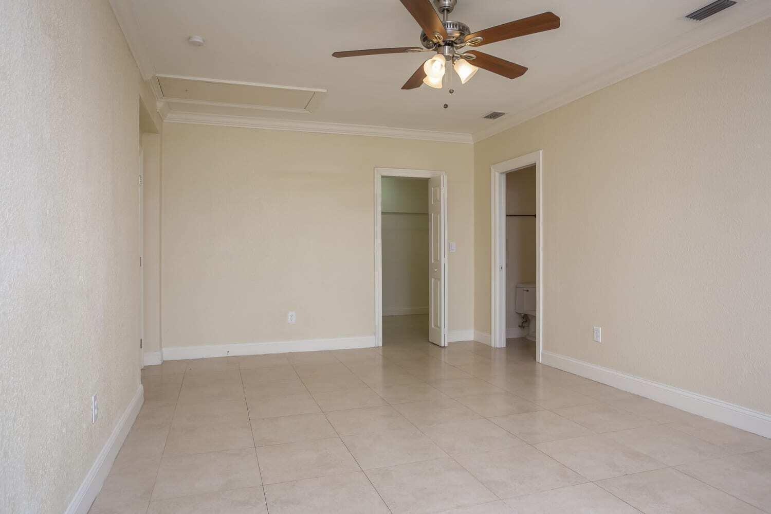 An empty room with beige tile flooring, a ceiling fan, and two open doorways — MIAMI, FL