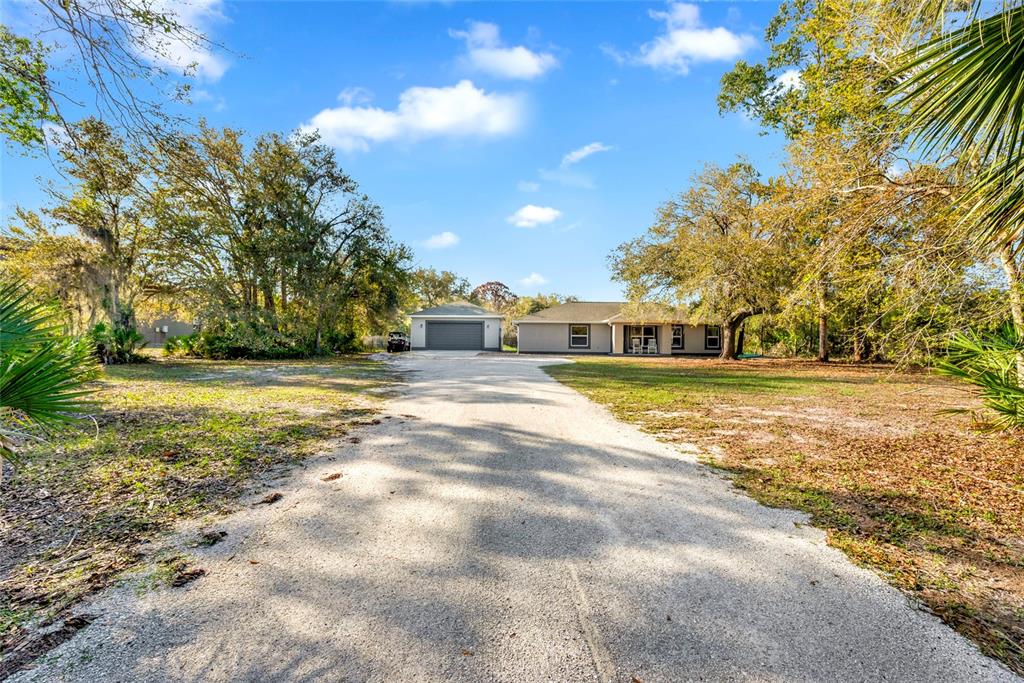 A gravel driveway leads to a detached garage and a single-story house among trees — 1811 BUTCH CASSIDY TRAIL, WIMAUMA, FL