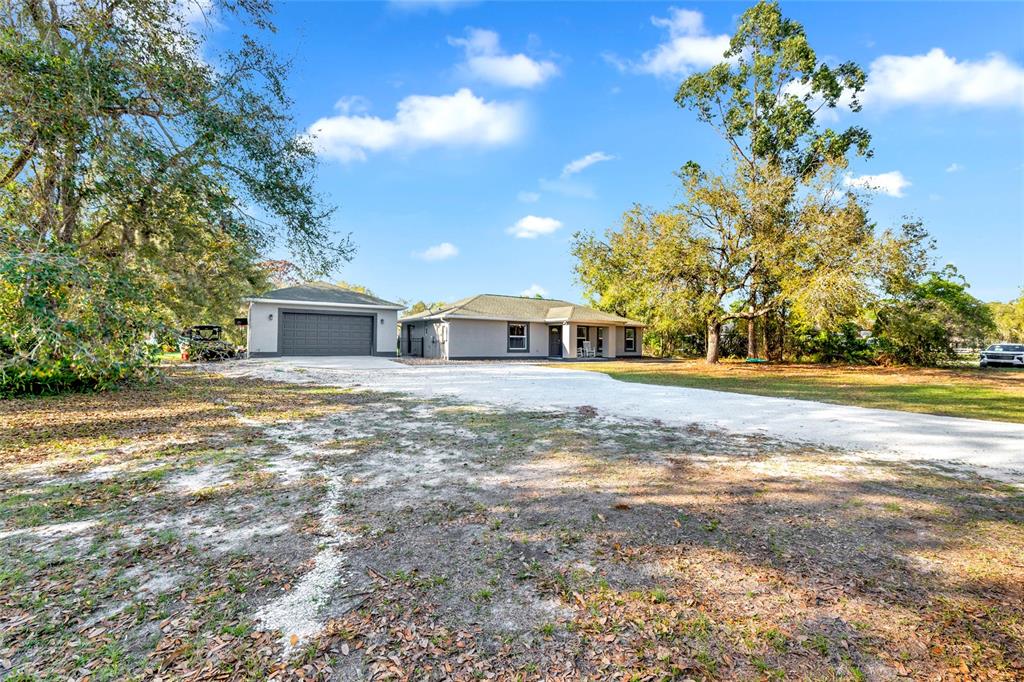 A single-story house with an attached garage sits on a large, sandy, tree-lined lot — 1811 BUTCH CASSIDY TRAIL, WIMAUMA, FL