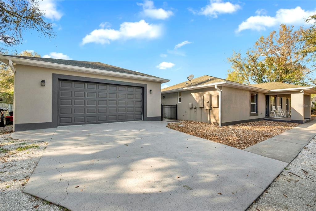 A beige house with a gray garage door, concrete driveway, and a gravel yard — 1811 BUTCH CASSIDY TRAIL, WIMAUMA, FL