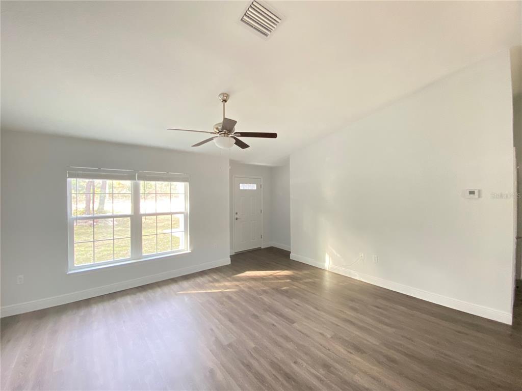 An empty living room features light gray walls, wood-look flooring, a ceiling fan, and a window — 9205 N ELKCAMP BOULEVARD, CITRUS SPRINGS, FL