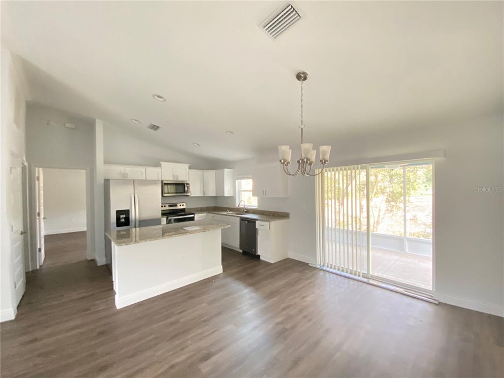 A kitchen with white cabinets, granite countertops, and stainless steel appliances opens to a dining area — 9205 N ELKCAMP BOULEVARD, CITRUS SPRINGS, FL