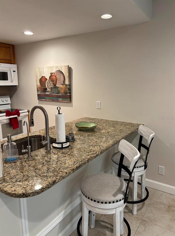 A kitchen island with a granite countertop, stainless steel sink, and two bar stools — 36750 US HIGHWAY 19 N UNIT 9-123, PALM HARBOR, FL
