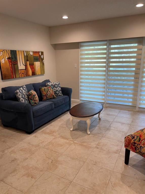 A living room features a blue sofa, a wooden coffee table, and large sliding glass doors — 36750 US HIGHWAY 19 N UNIT 9-123, PALM HARBOR, FL