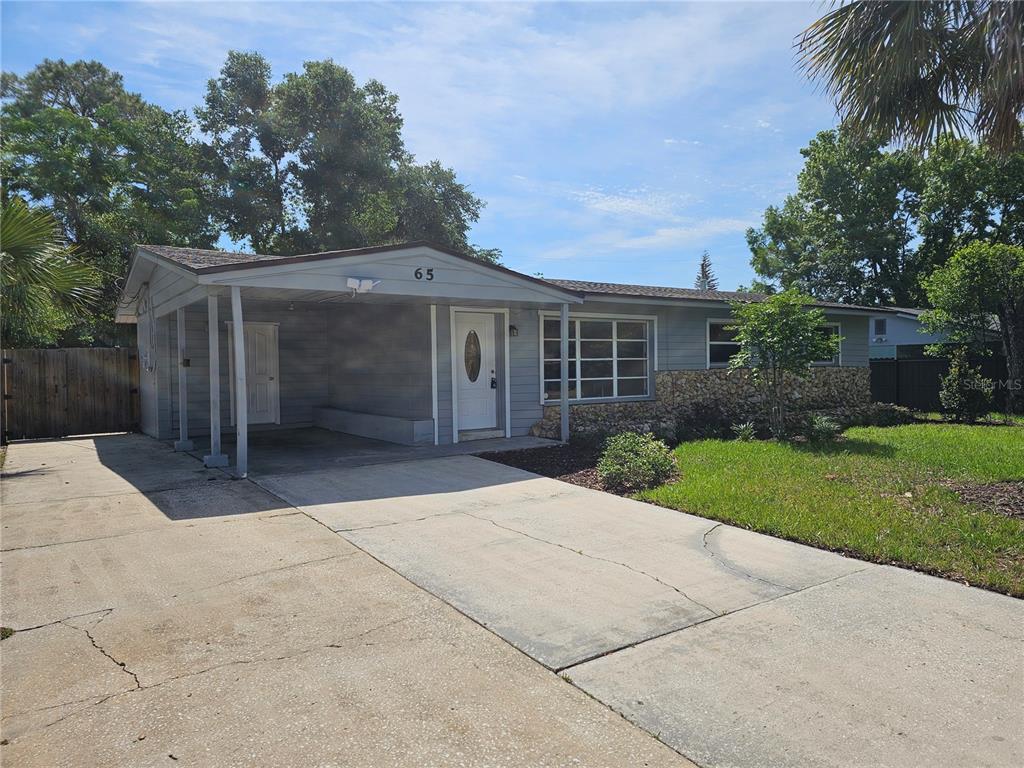 A single-story house with a carport, concrete driveway, and stone facade under a blue sky — 65 S DEVON AVENUE, WINTER SPRINGS, FL