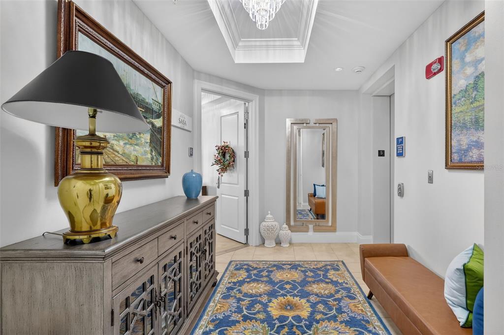 A hallway features a console table, a bench, a patterned rug, and a ceiling chandelier — 130 RIVIERA DUNES WAY UNIT 506, PALMETTO, FL