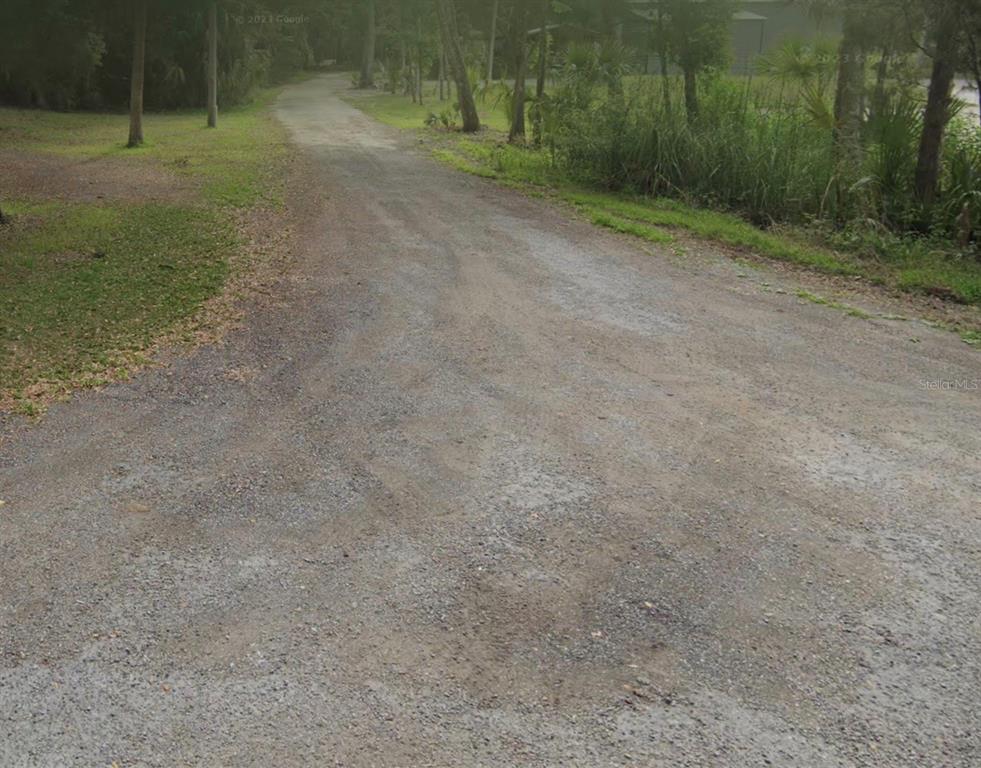 A gravel driveway leads through a wooded area toward a house in the distance — 10465 W LARCHWOOD STREET, HOMOSASSA, FL