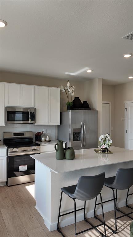 A modern kitchen features white cabinets, stainless steel appliances, and a central island with seating — 5160 NATALIA DRIVE, ST CLOUD, FL