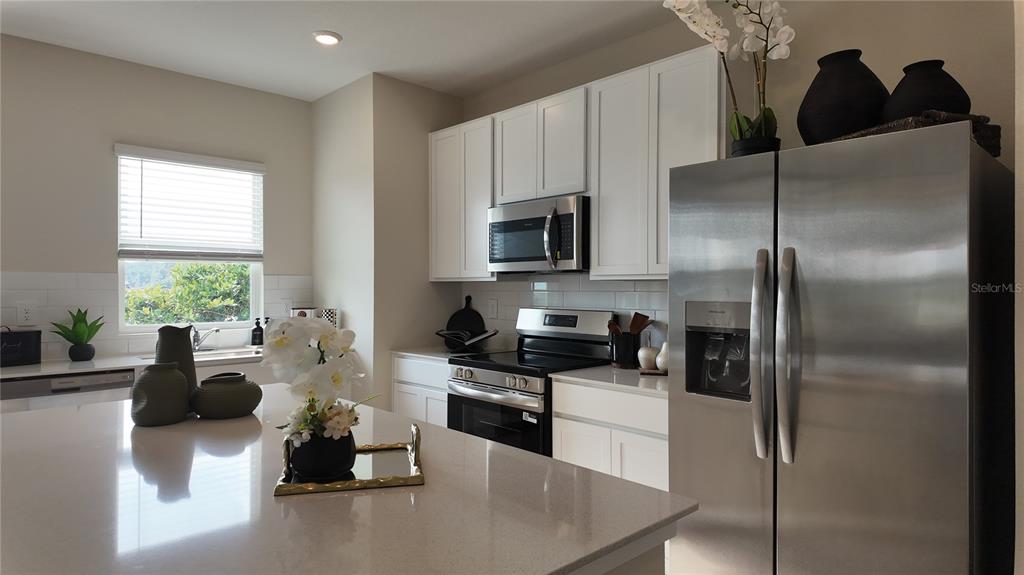 A kitchen features white cabinets, stainless steel appliances, and a large quartz-topped island — 5160 NATALIA DRIVE, ST CLOUD, FL