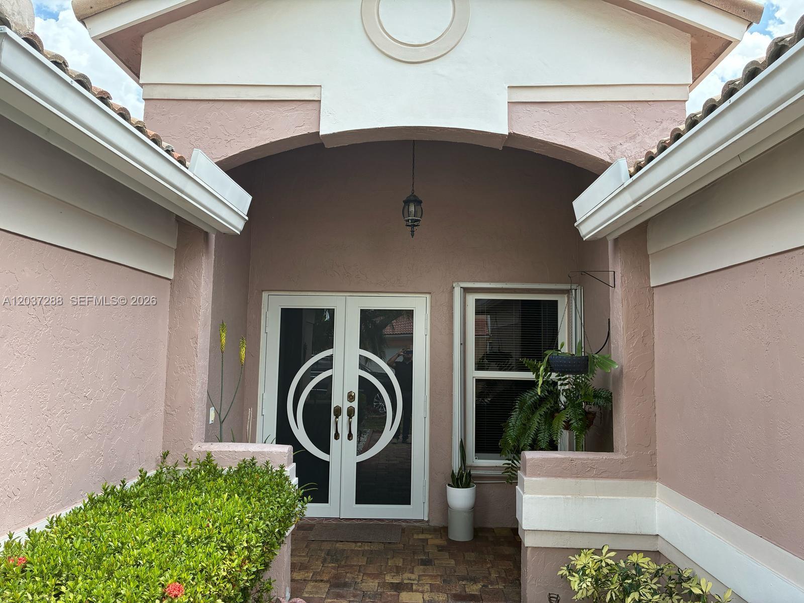 The exterior entrance features a pink stucco facade, double glass doors, and a tiled porch — 1412 NW 129th Terrace, Sunrise FL 33323, SUNRISE, FL