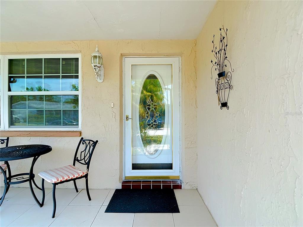 A covered porch features a white front door with an oval glass insert and furniture — 8944 LEDGESTONE LANE, PORT RICHEY, FL