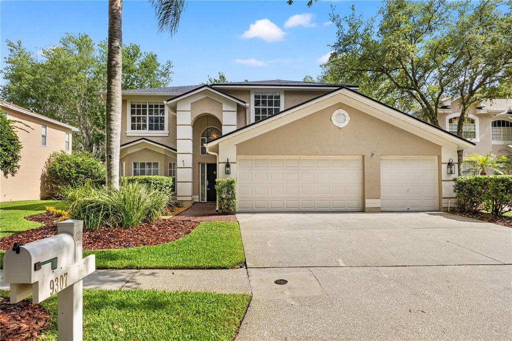 A two-story house with a beige stucco exterior, a three-car garage, and a landscaped yard — 9307 POPLAR CREEK COURT, TAMPA, FL