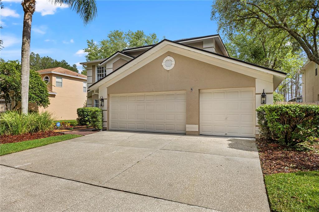 A two-car garage with a concrete driveway sits in front of a tan suburban home — 9307 POPLAR CREEK COURT, TAMPA, FL