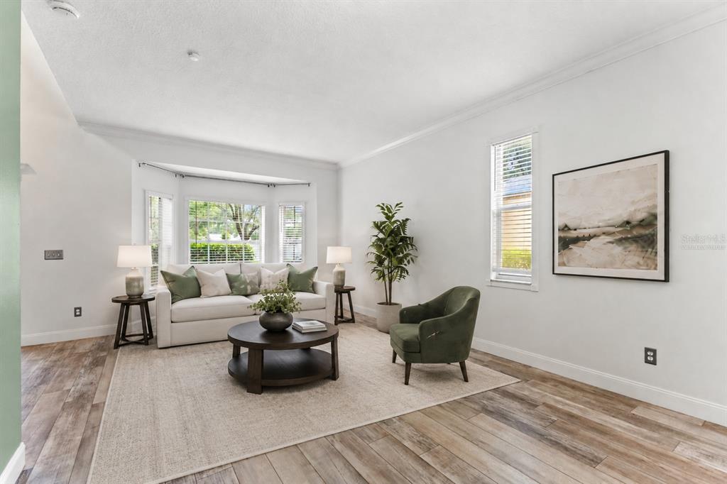 A bright living room with a white sofa, green armchair, and wood-look tile flooring — 9307 POPLAR CREEK COURT, TAMPA, FL