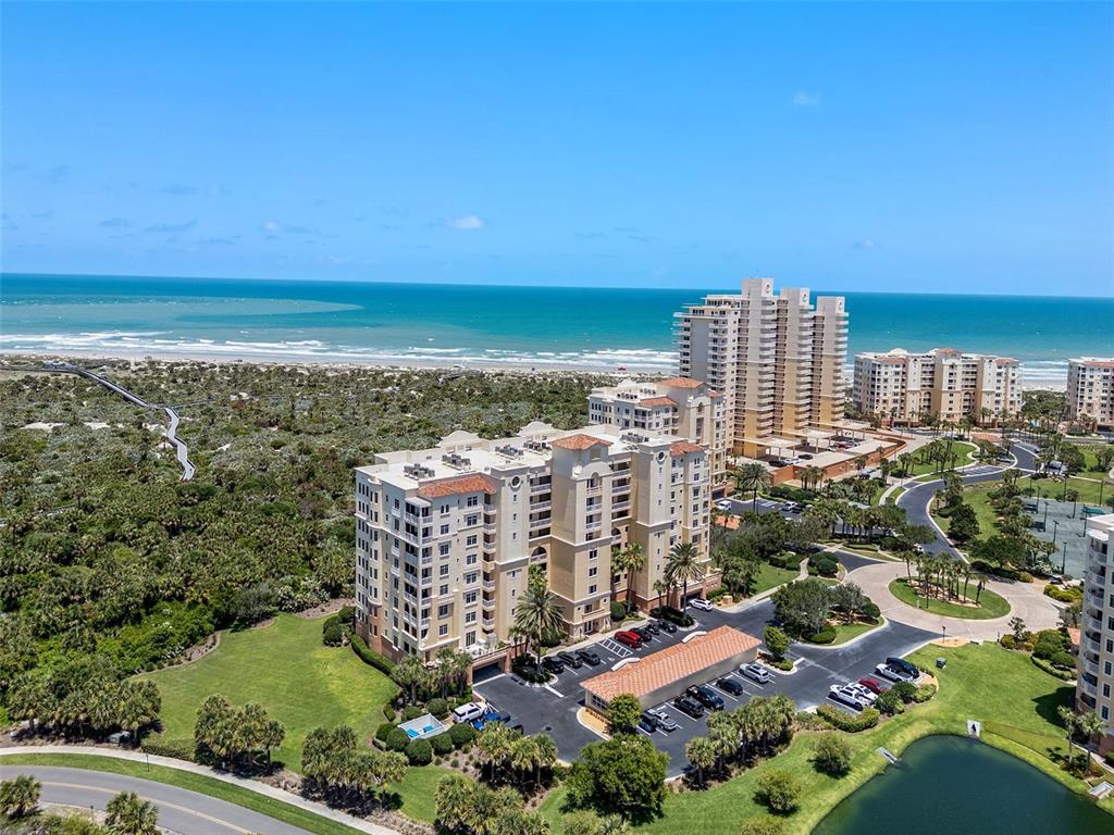 An aerial view shows a multi-story residential building near a beach and ocean — 261 MINORCA BEACH WAY UNIT 606, NEW SMYRNA BEACH, FL