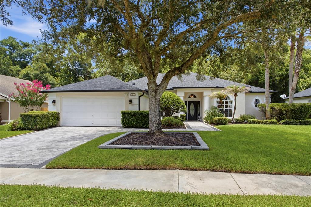 A single-story house with a paved driveway, a large tree, and a white garage door — 223 BLUE CREEK DRIVE, WINTER SPRINGS, FL