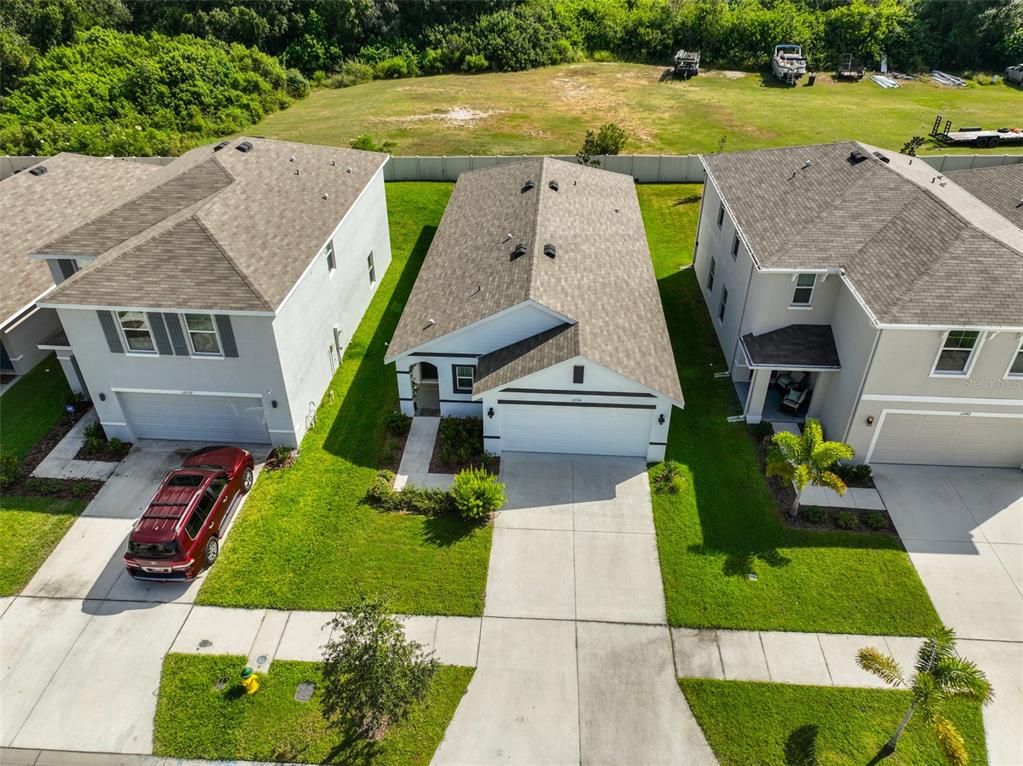 An aerial view shows three suburban houses with driveways, lawns, and a shared backyard fence — 12136 LILY MAGNOLIA LANE, RIVERVIEW, FL