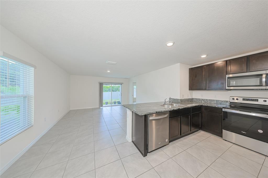 A kitchen with dark cabinets and granite countertops opens into a tiled living area — 12136 LILY MAGNOLIA LANE, RIVERVIEW, FL