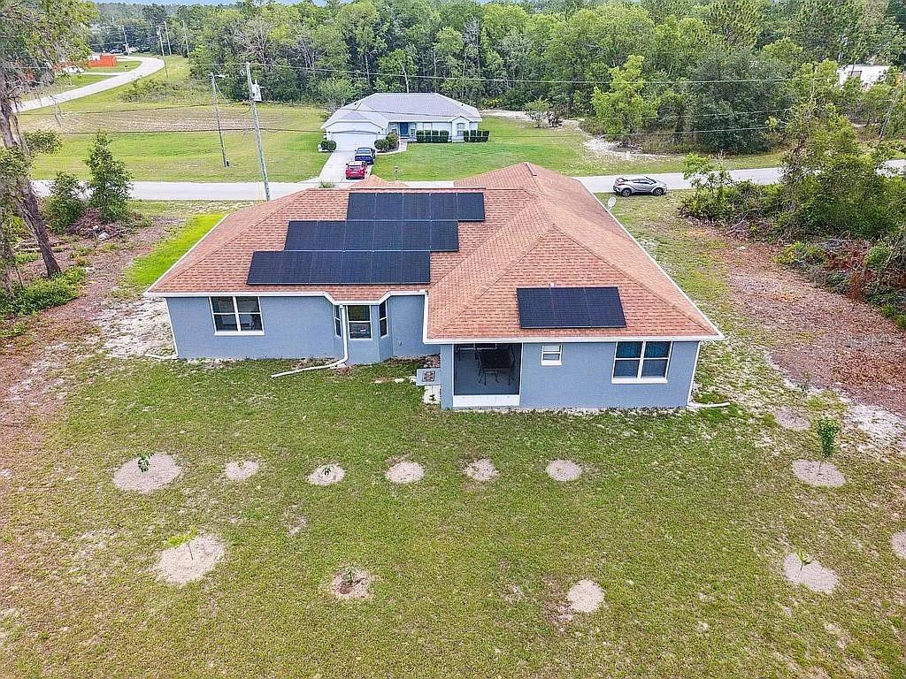 An aerial view of a blue house with solar panels on a brown shingled roof — 8628 SW 133RD LANE ROAD, OCALA, FL