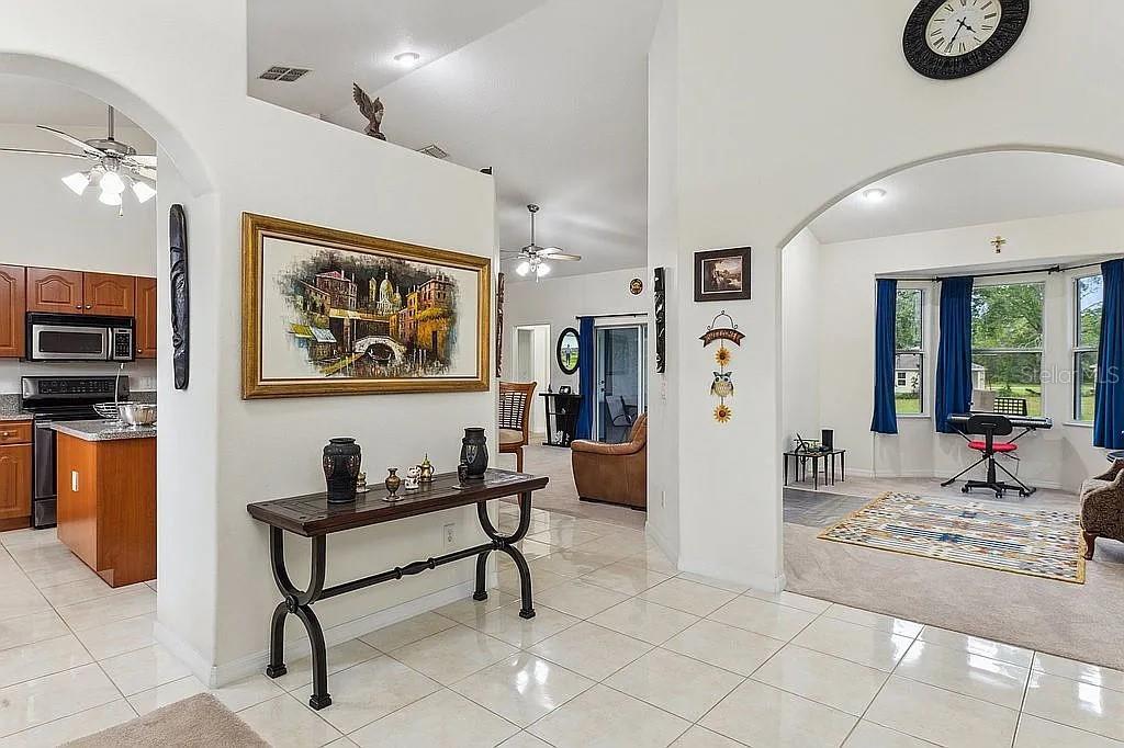 An open-concept living area features tiled floors, arched doorways, a console table, and a kitchen — 8628 SW 133RD LANE ROAD, OCALA, FL