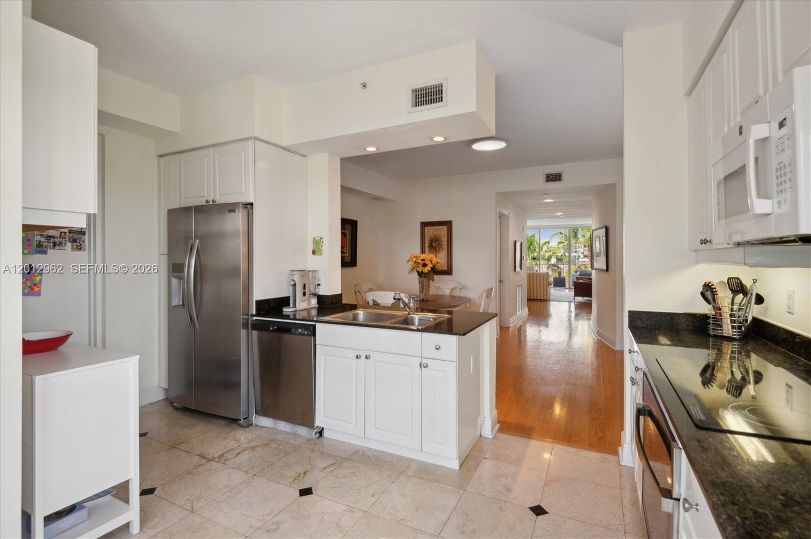 A kitchen with white cabinets, stainless steel appliances, and dark countertops opens to a dining area — 701 Crandon Blvd # 1, Key Biscayne FL 33149, KEY BISCAYNE, FL