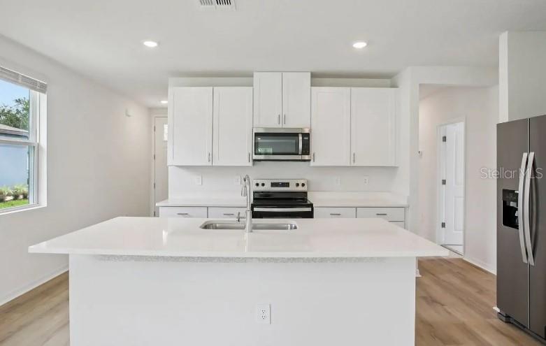 A modern kitchen features white cabinets, a central island with a sink, and stainless appliances — 153 CANOE BEND AVENUE, NOKOMIS, FL