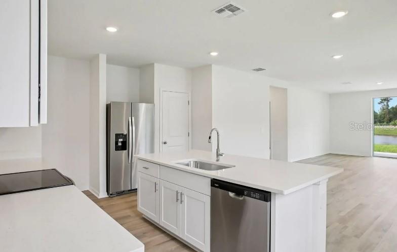 A kitchen features white cabinets, stainless steel appliances, a center island, and light wood flooring — 153 CANOE BEND AVENUE, NOKOMIS, FL
