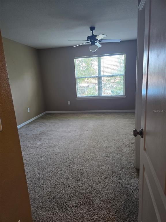 An empty bedroom features beige walls, tan carpeting, a ceiling fan, and a window with blinds — 2157 BROADWAY VIEW AVENUE, BRANDON, FL