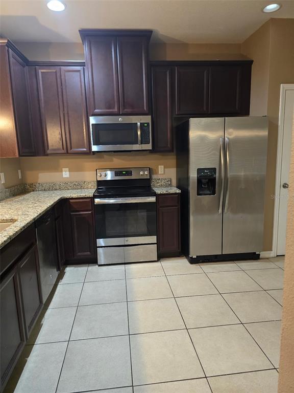 A kitchen features dark wood cabinets, granite countertops, stainless steel appliances, and light tile flooring — 2157 BROADWAY VIEW AVENUE, BRANDON, FL