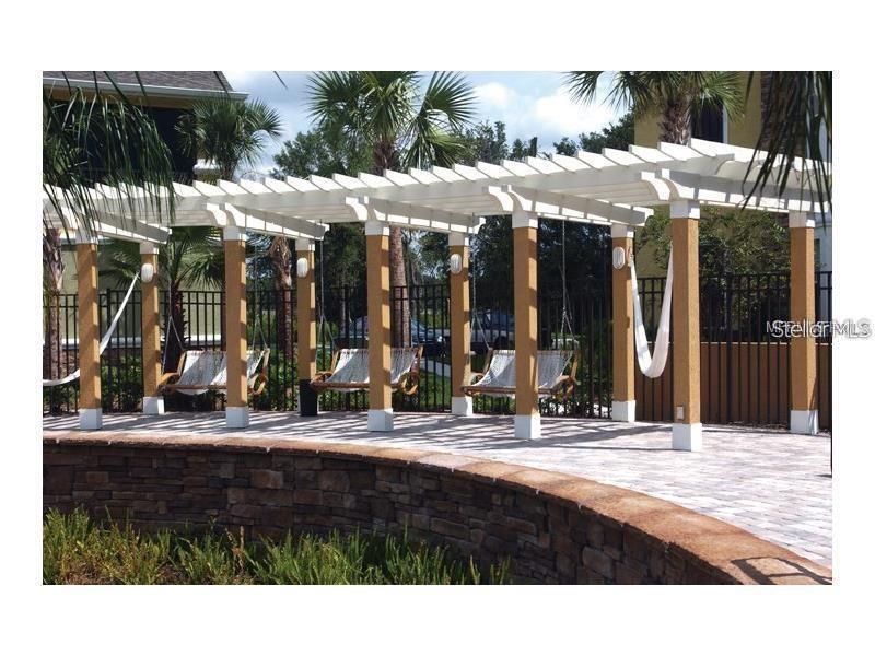 A white pergola with hanging swings sits on a paved patio beside a stone wall — 10019 COURTNEY PALMS BOULEVARD UNIT 201, TAMPA, FL