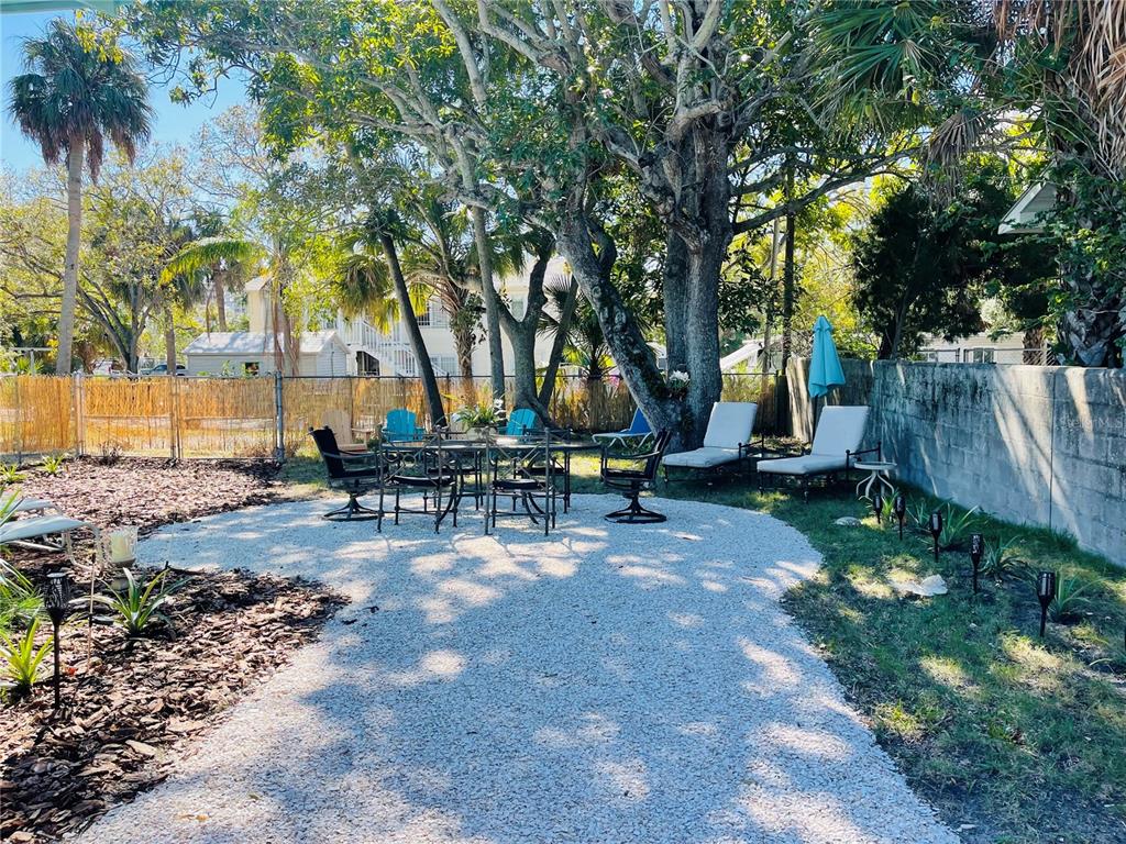 A gravel patio features a dining set and lounge chairs under large trees in a yard — 1270 5TH STREET, SARASOTA, FL