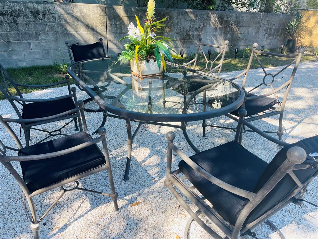 A glass-topped patio table with six chairs sits on a gravel surface outdoors — 1270 5TH STREET, SARASOTA, FL