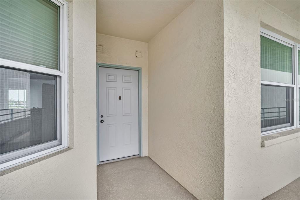 A white front door is recessed into a beige stucco entryway with two windows — 7932 SAILBOAT KEY BOULEVARD S UNIT 402, SOUTH PASADENA, FL