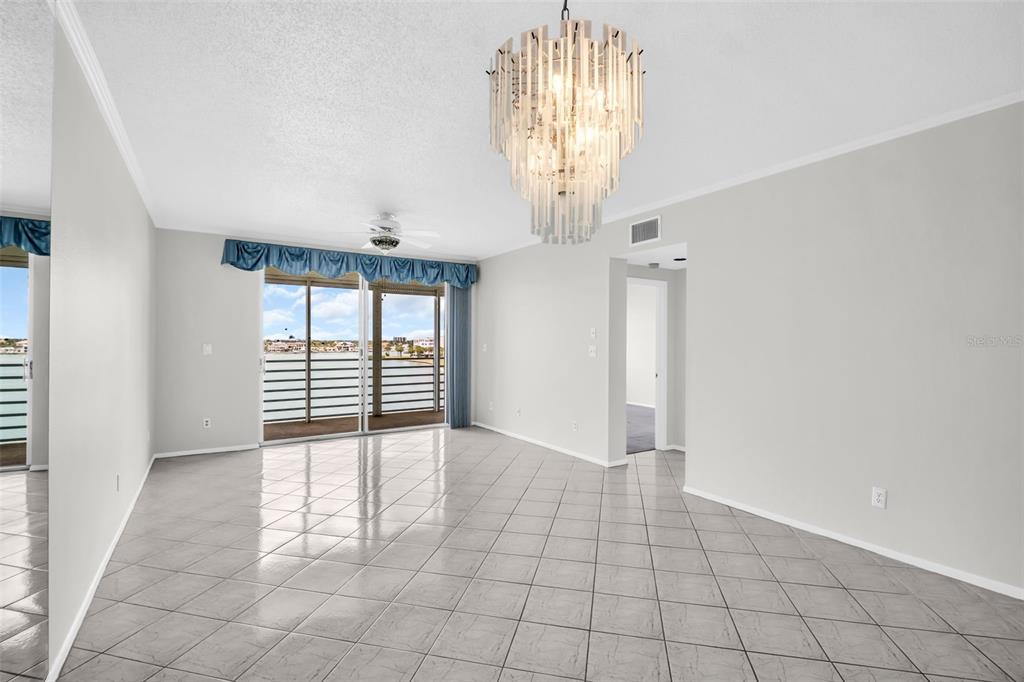 A bright living room features light-colored tile flooring, a crystal chandelier, and sliding glass doors — 7932 SAILBOAT KEY BOULEVARD S UNIT 402, SOUTH PASADENA, FL