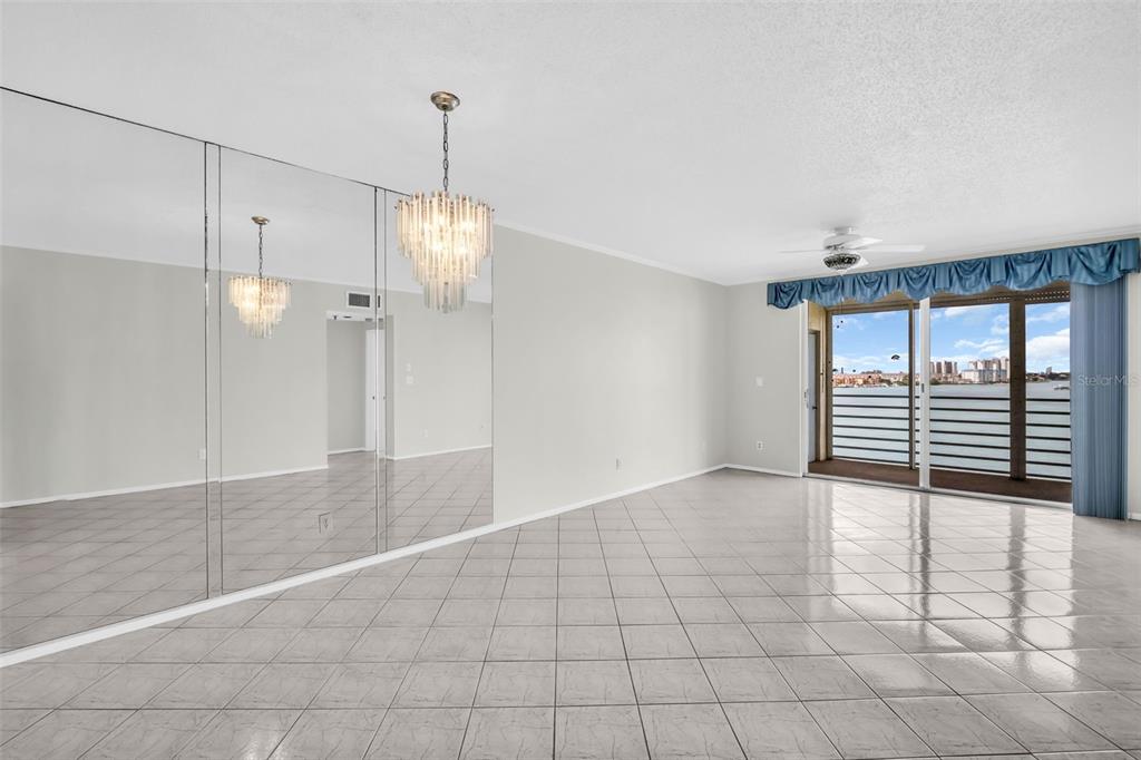 A bright living room features tiled floors, a mirrored wall, a crystal chandelier, and balcony access — 7932 SAILBOAT KEY BOULEVARD S UNIT 402, SOUTH PASADENA, FL