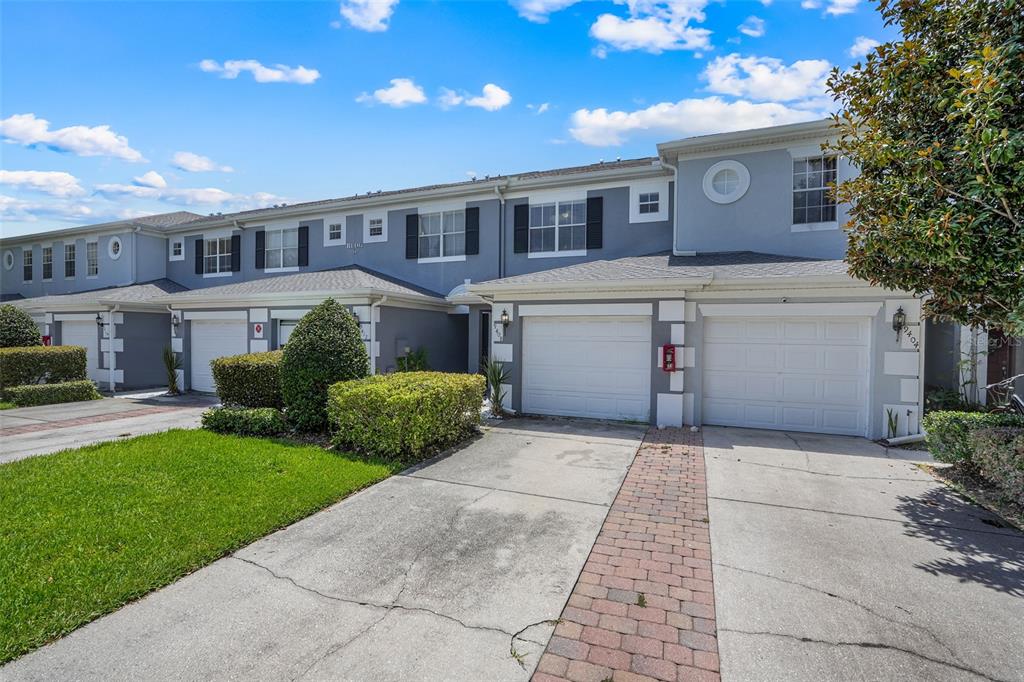 A two-story townhouse exterior features a gray facade, white garage doors, and a paved driveway — 9408 FLOWERING COTTONWOOD ROAD, ORLANDO, FL