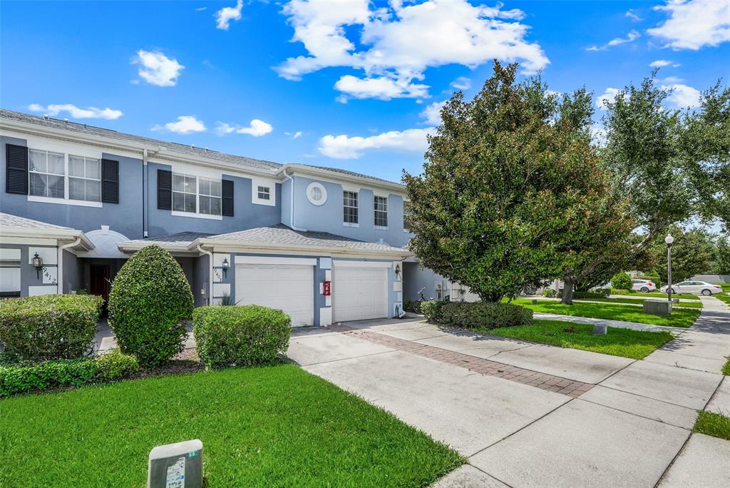 A two-story townhouse with a blue exterior, two garage doors, and a front lawn — 9408 FLOWERING COTTONWOOD ROAD, ORLANDO, FL