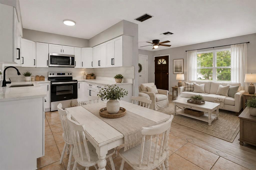 An open-concept kitchen and living room featuring white cabinetry, a dining table, and neutral furniture — 1532 N NORMANDY BOULEVARD, DELTONA, FL