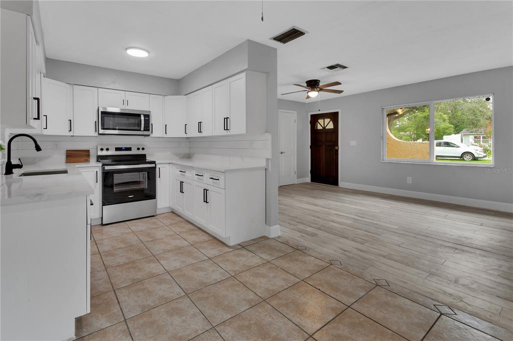 A kitchen with white cabinets and tile flooring opens into a living area with wood floors — 1532 N NORMANDY BOULEVARD, DELTONA, FL