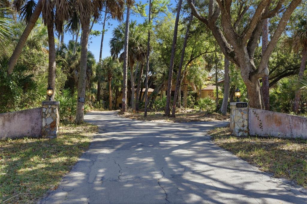 A paved driveway leads toward a house partially obscured by trees and stone entrance pillars — 1066 CONOVER STREET, PORT CHARLOTTE, FL