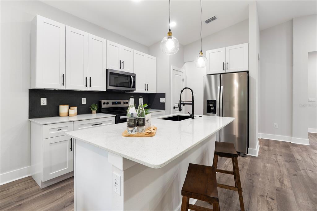 A modern kitchen features white cabinets, a quartz island, stainless steel appliances, and dark flooring — 12248 SW 96TH LANE, DUNNELLON, FL