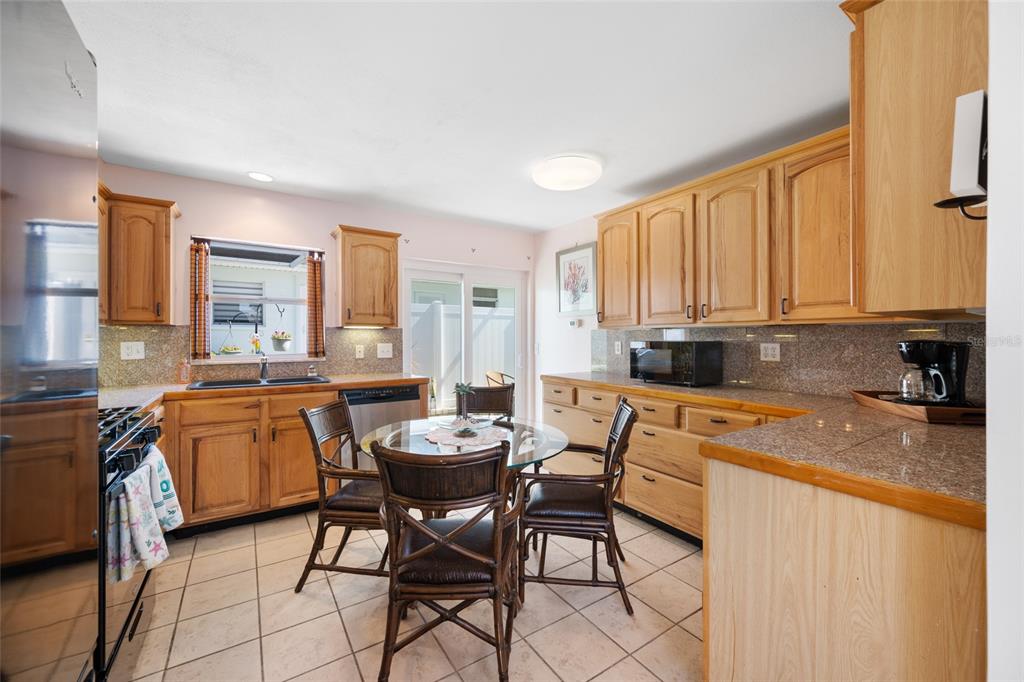 A kitchen features light wood cabinets, granite countertops, tile flooring, and a small dining set — 12400 PARK BLVD UNIT 623, SEMINOLE, FL