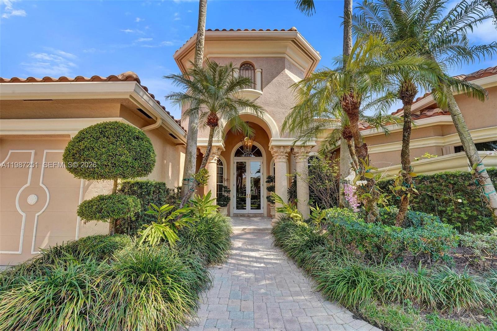 The exterior of a beige stucco house features a stone walkway, arched entryway, and palm trees — 10813 Blackhawk St, Plantation FL 33324, PLANTATION, FL