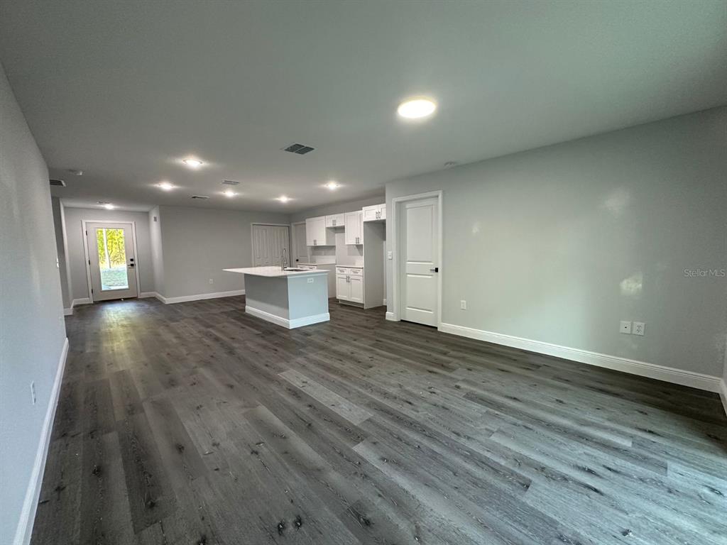 An open-concept kitchen and living area features gray wood-look flooring and white cabinetry — 15 BAHIA COURT TRACK, OCALA, FL
