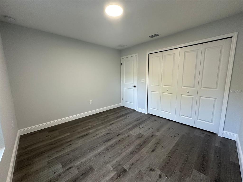 An empty bedroom features gray walls, dark wood-look flooring, a closet, and a white door — 15 BAHIA COURT TRACK, OCALA, FL